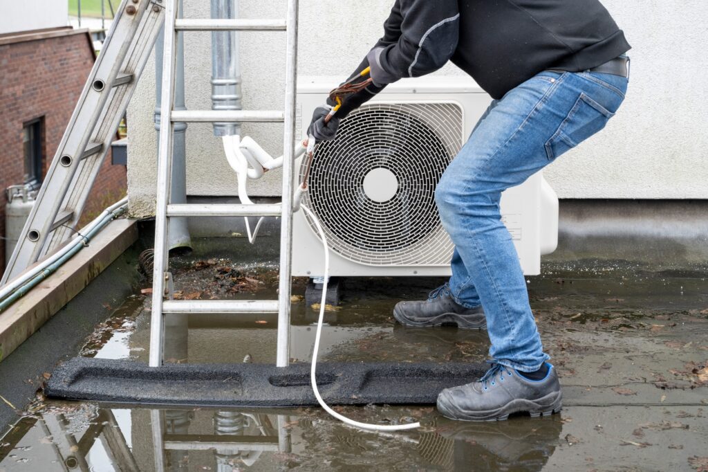 A technician servicing an outdoor AC unit on a rooftop.