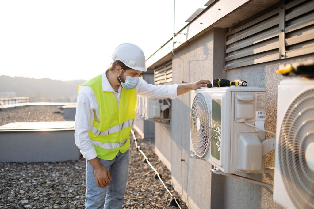 Craftsman in face mask cleaning air conditioner on rooftop