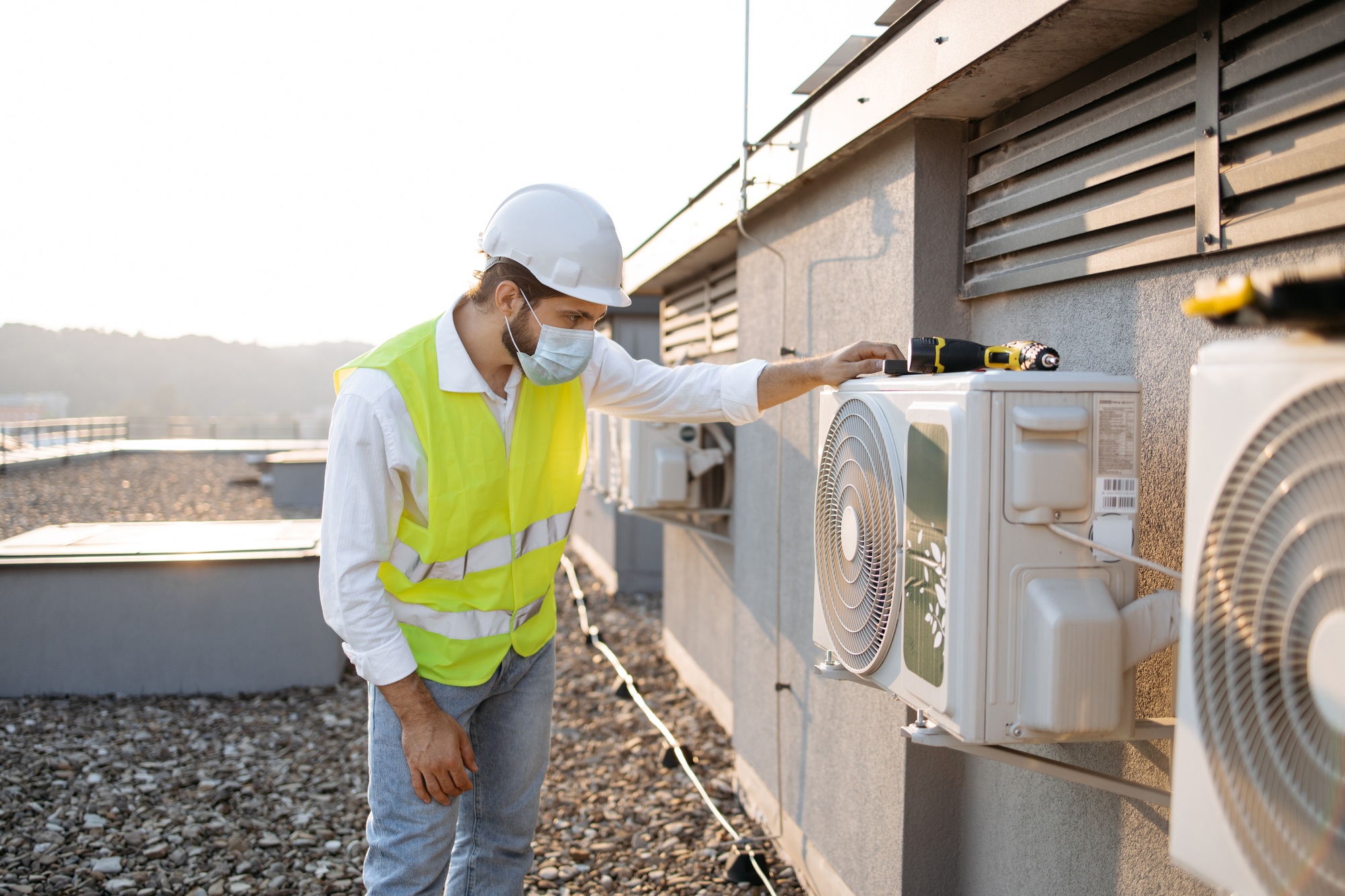 Craftsman in face mask cleaning air conditioner on rooftop